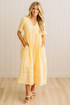 Woman wearing a yellow lace dress standing against a white wall.