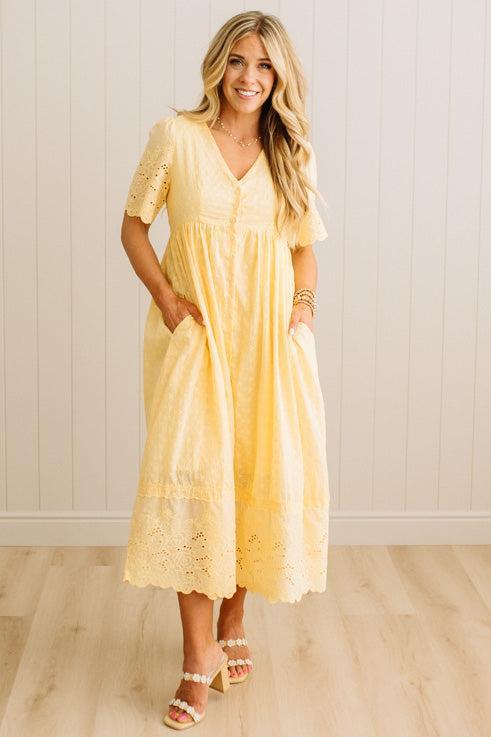 Woman wearing a yellow lace dress standing against a white wall.