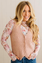 Woman wearing a pink vest over a floral long-sleeve shirt with a neutral background