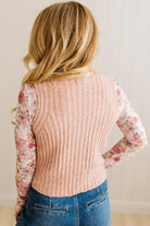 Person wearing a ribbed sweater vest over a floral shirt with blue jeans against a neutral background