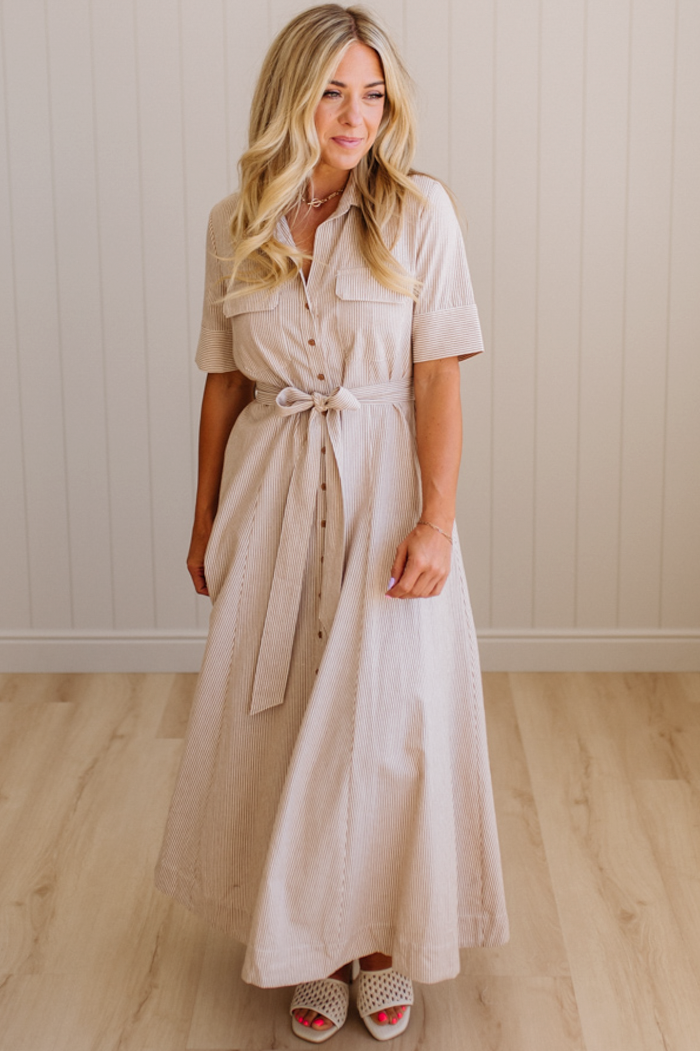 Woman wearing a beige dress standing against a plain wall.