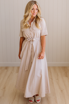 Woman wearing a beige dress standing against a plain wall.