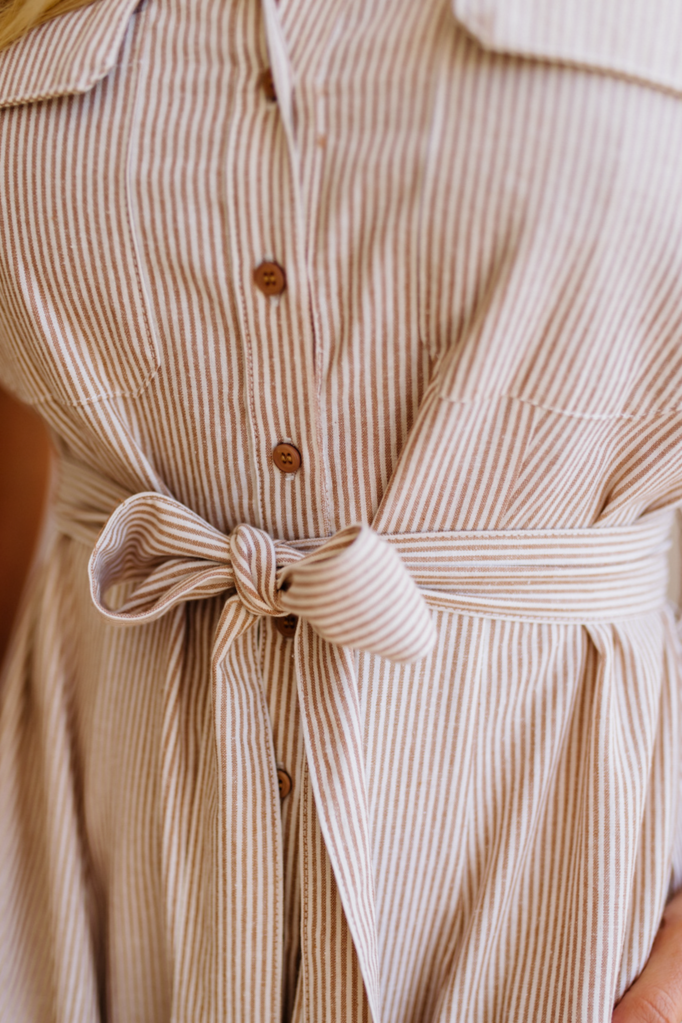 Close-up of a beige and brown striped dress with a tie waist.