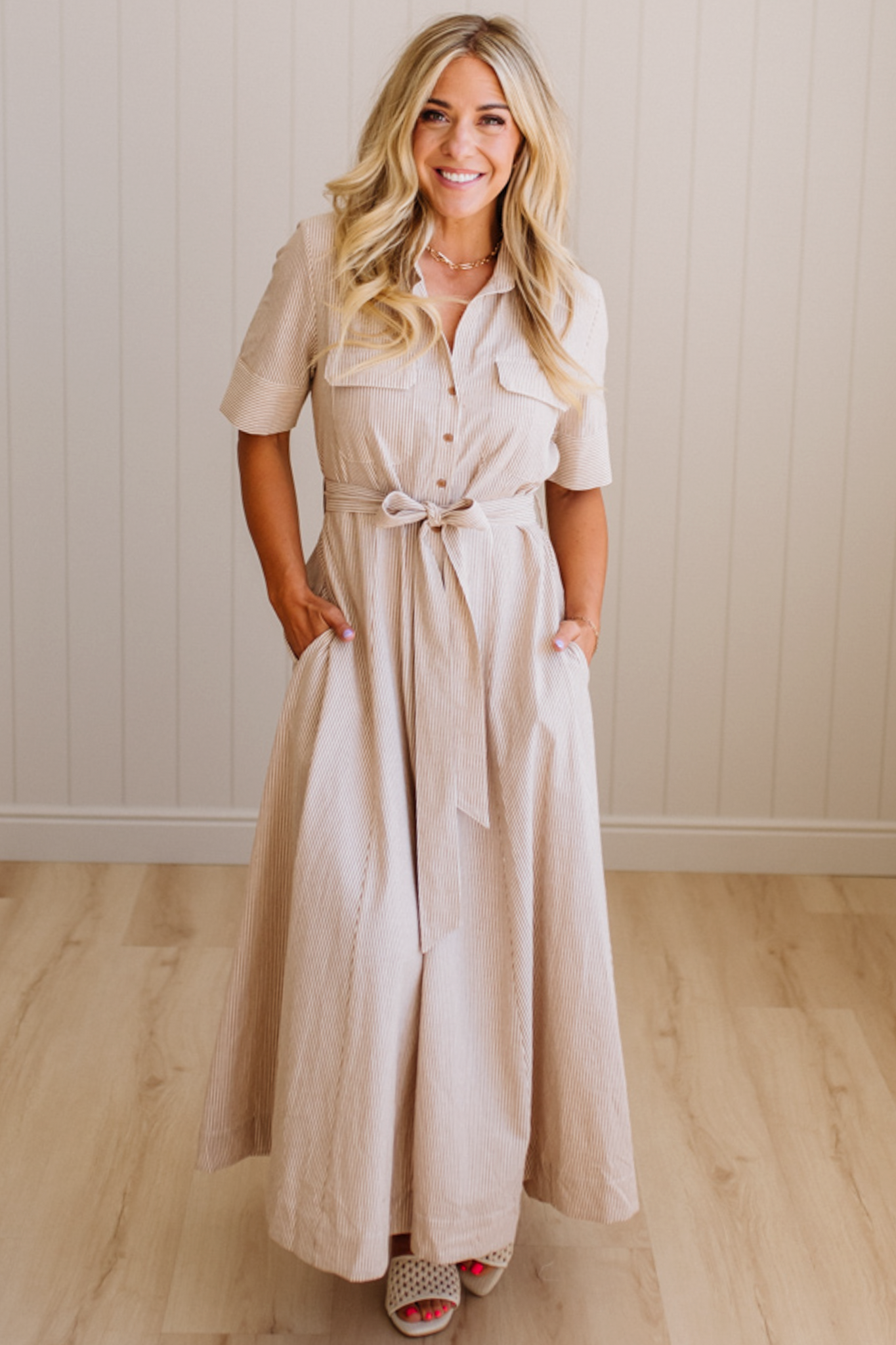 Woman wearing a beige dress standing against a plain wall.