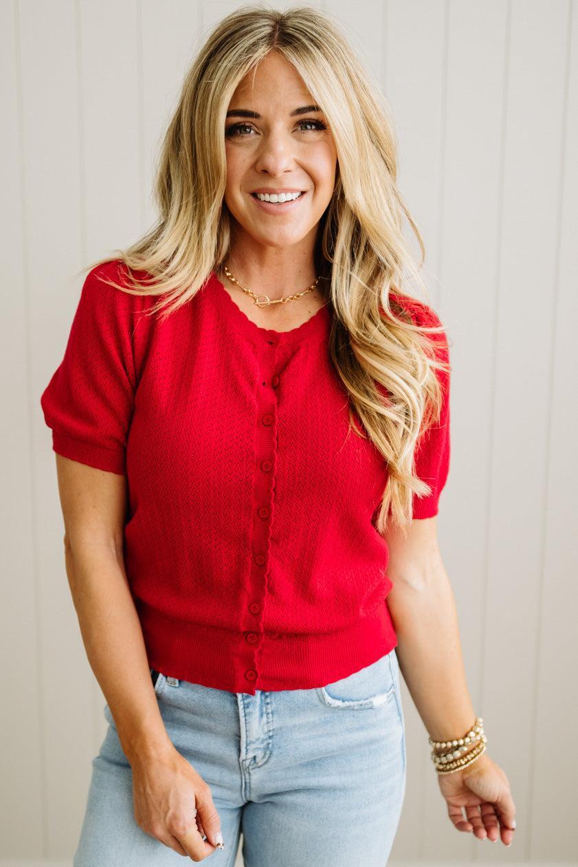 Woman wearing a red top and light blue jeans against a plain background