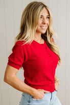 Woman wearing a red short-sleeve top and light blue jeans against a neutral background