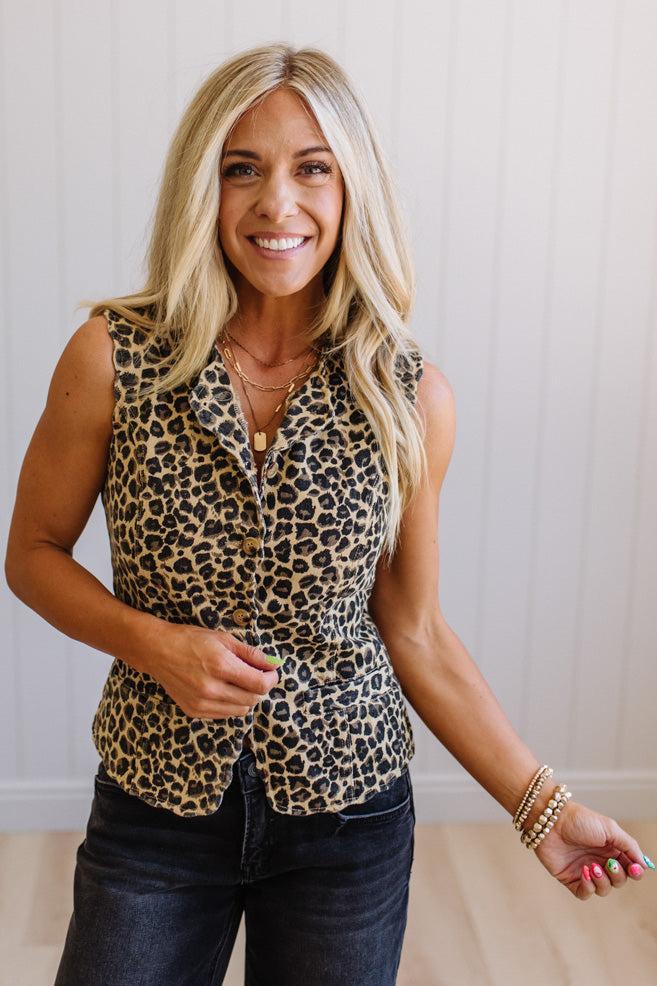 Woman wearing a leopard print sleeveless top and dark jeans against a neutral background