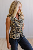 Woman wearing a leopard print sleeveless top and dark jeans indoors.