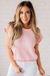 Blonde woman wearing a textured pink sweater with scalloped red trim.