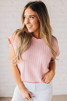 Blonde woman wearing a textured pink sweater with scalloped red trim.