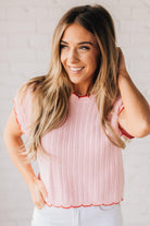 Blonde woman wearing a textured pink sweater with scalloped red trim.