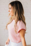 Blonde woman wearing a textured pink sweater with scalloped red trim.