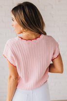 Blonde woman wearing a textured pink sweater with scalloped red trim.