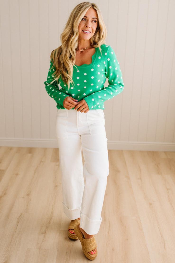 Blonde woman wearing a long sleeve sweater with scalloped square neckline in green with white dots.