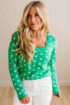 Blonde woman wearing a long sleeve sweater with scalloped square neckline in green with white dots.