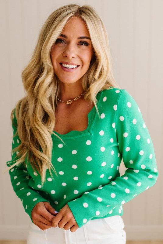 Blonde woman wearing a long sleeve sweater with scalloped square neckline in green with white dots.