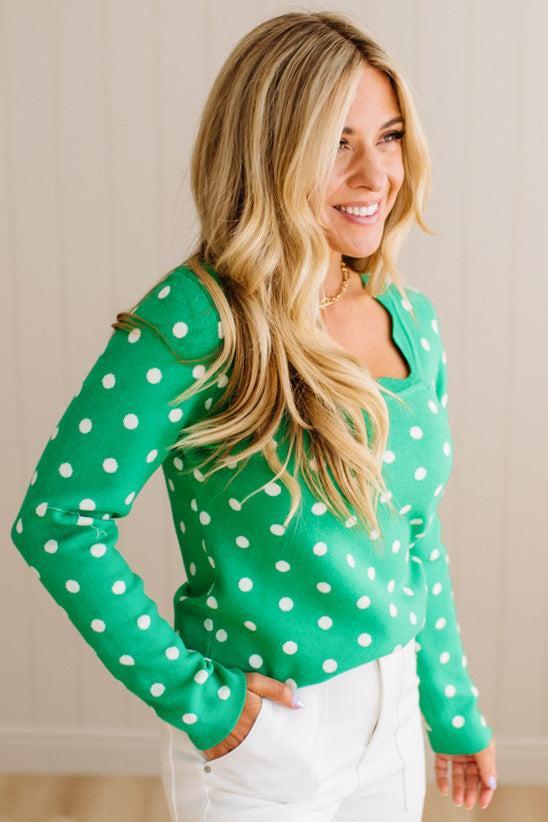 Blonde woman wearing a long sleeve sweater with scalloped square neckline in green with white dots.