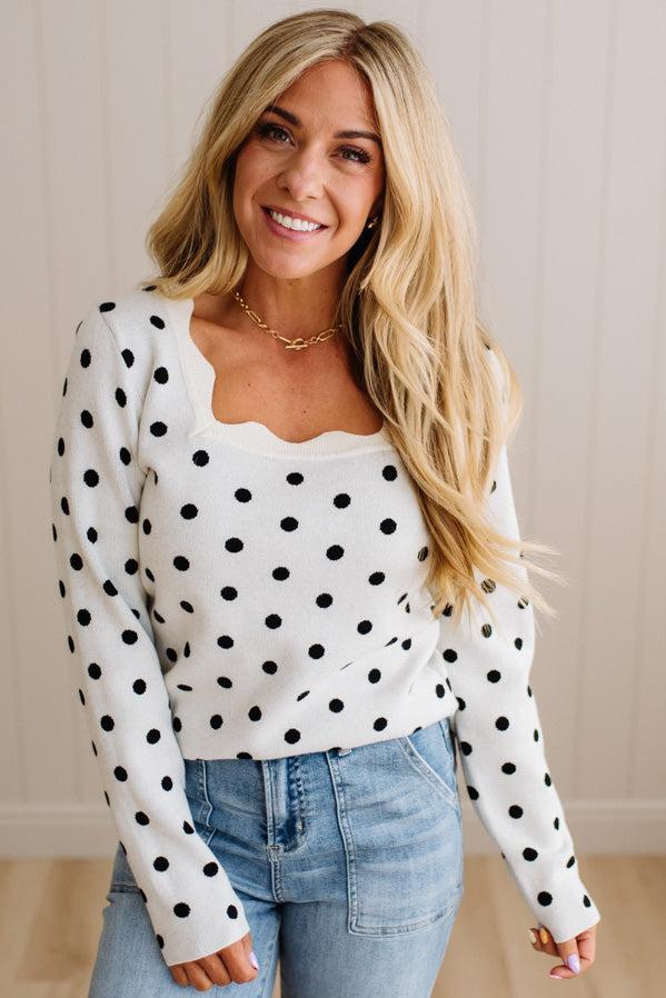 Blonde woman wearing a long sleeve sweater with scalloped square neckline in white with black dots.