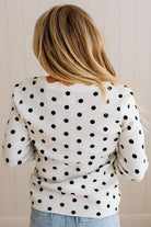 Blonde woman wearing a long sleeve sweater with scalloped square neckline in white with black dots.