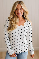 Blonde woman wearing a long sleeve sweater with scalloped square neckline in white with black dots.
