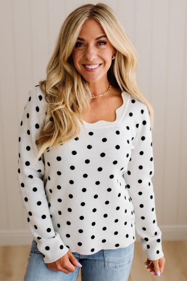 Blonde woman wearing a long sleeve sweater with scalloped square neckline in white with black dots.