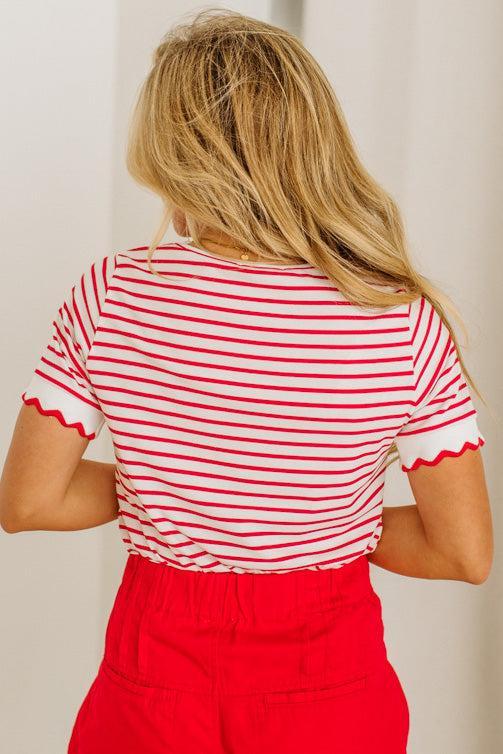 Person wearing a red and white striped shirt with scalloped edges and red pants against a plain background