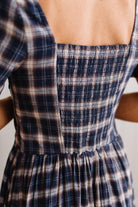 Close-up of the back of a smocked dress with a navy, beige, and white plaid pattern, worn by a model.