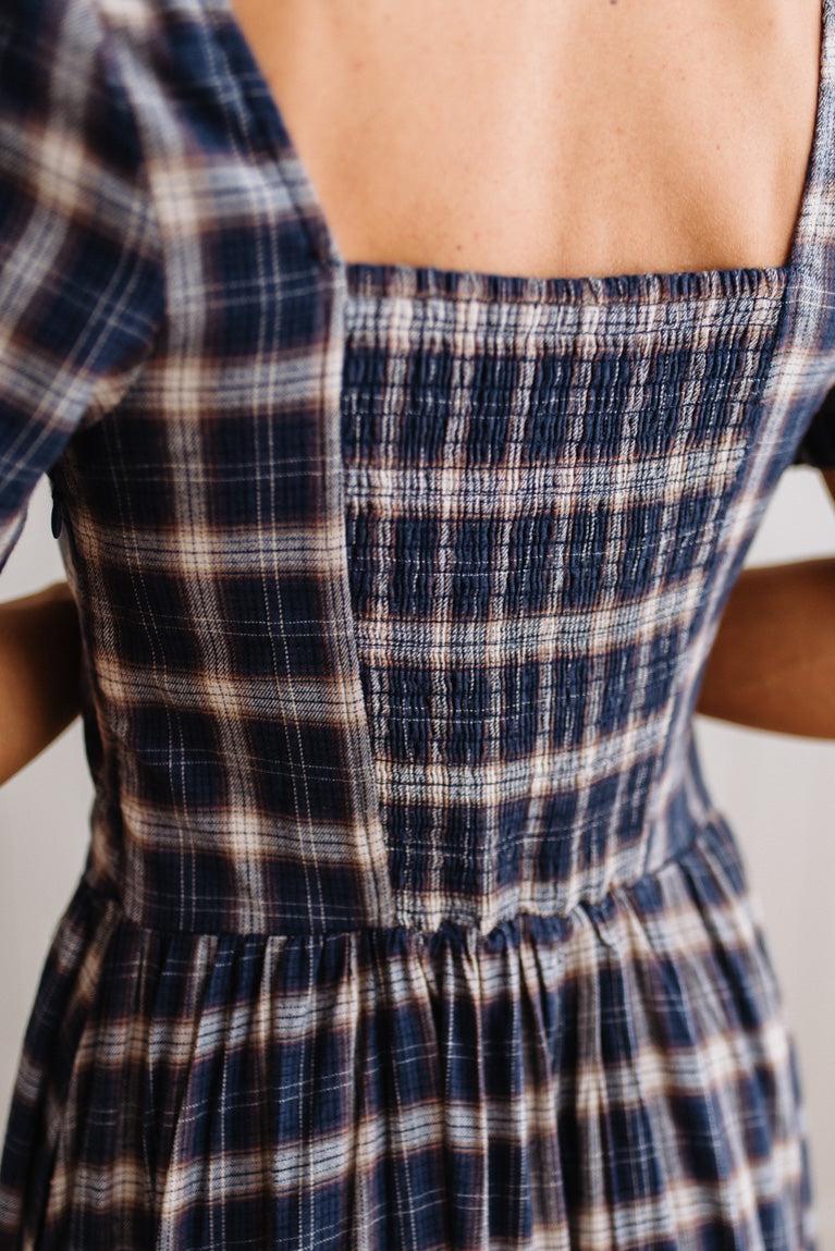 Close-up of the back of a smocked dress with a navy, beige, and white plaid pattern, worn by a model.