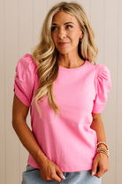 Woman wearing a pink top with puff sleeves against a neutral background