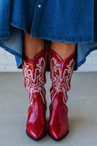 Red cowboy boots with white patterns worn with a denim skirt.