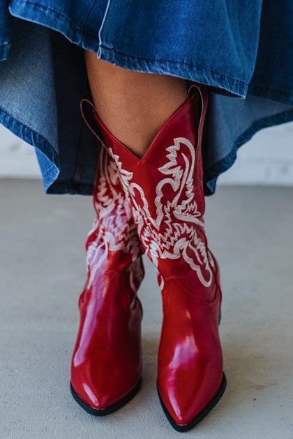 Red cowboy boots with white patterns worn by a person in a blue denim outfit.