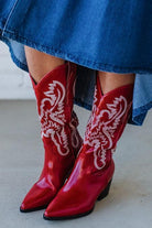 Red cowboy boots with white patterns worn with a blue denim skirt.