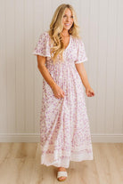 Woman wearing a floral dress standing against a light wooden paneled wall.