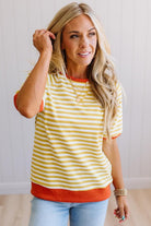 Blonde woman wearing light jeans and a mustard yellow with white stiripe short sleeve top, that also has a dark orange contrast trim.