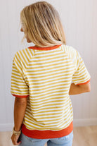Blonde woman wearing light jeans and a mustard yellow with white stiripe short sleeve top, that also has a dark orange contrast trim.