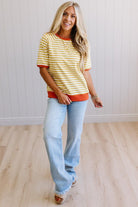 Blonde woman wearing light jeans and a mustard yellow with white stiripe short sleeve top, that also has a dark orange contrast trim.