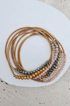 A stack of multi-strand beaded bracelets with gold-toned metal bands, displayed on a white ceramic plate over a light beige textured surface.