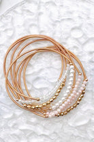 A close-up of a stack of gold and pearl beaded bracelets, on a textured surface.