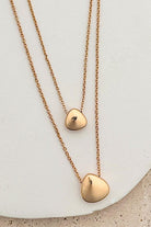 Two gold heart-shaped pendants on delicate chains against a light background