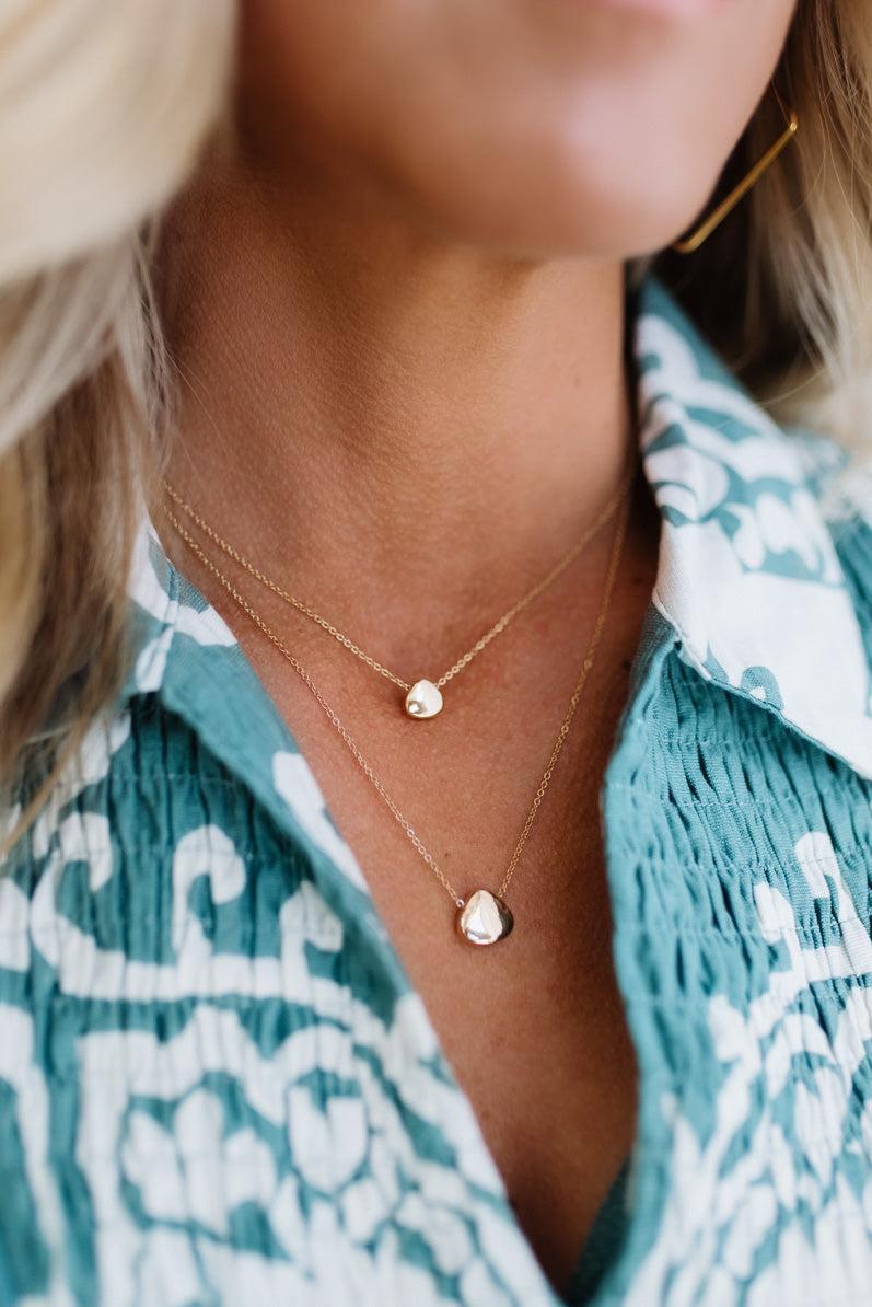 Close-up of a person wearing a gold necklace with heart pendants against a teal and white patterned garment.