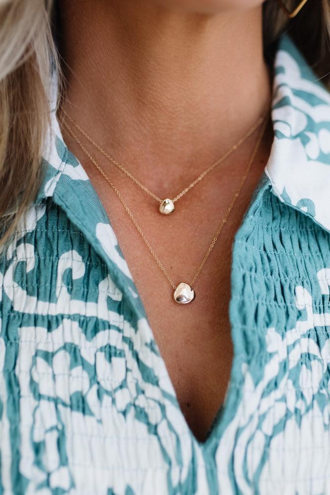 Close-up of a person wearing a gold necklace with a pendant against a patterned garment.