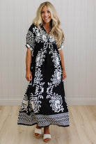 Woman wearing a black and white patterned dress against a white wall.