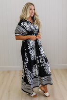 Woman wearing a black and white patterned dress standing against a white wall.