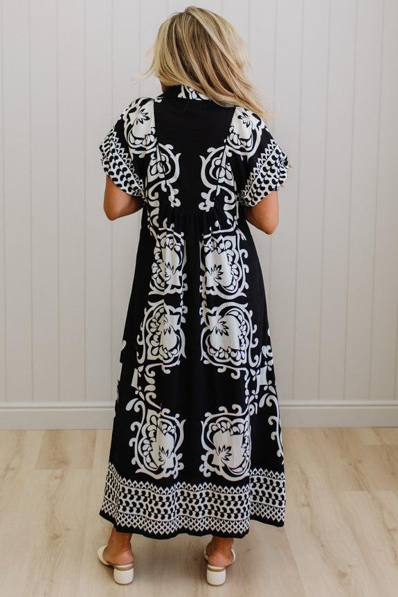 Woman wearing a black dress with white patterns in a minimal indoor setting
