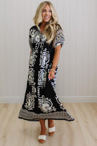 Woman wearing a black and white patterned dress standing against a white wall.