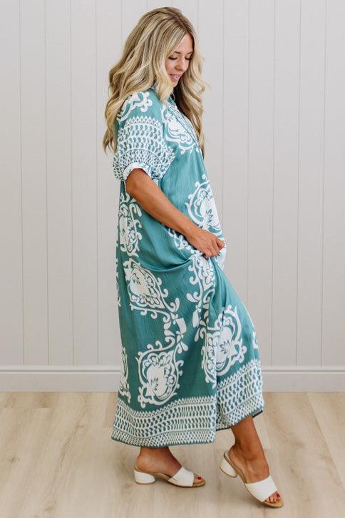 Woman wearing a teal and white patterned dress standing against a white paneled wall.