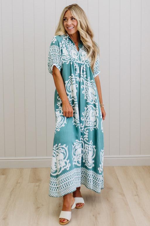 Woman wearing a teal and white patterned dress against a light wooden panel background