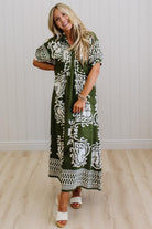 Woman wearing a green and white patterned dress standing against a white paneled wall.