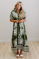 Woman wearing a green dress with white patterns against a white wall.