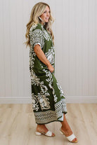 Woman wearing a green patterned dress standing against a white wall.